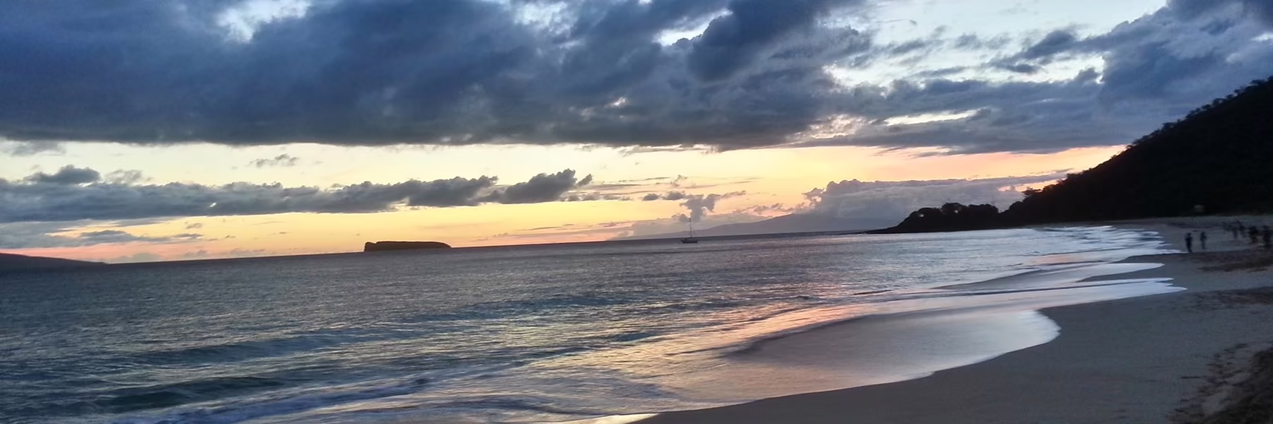 A wide sand beach at dusk, with a small island low on the horizon.